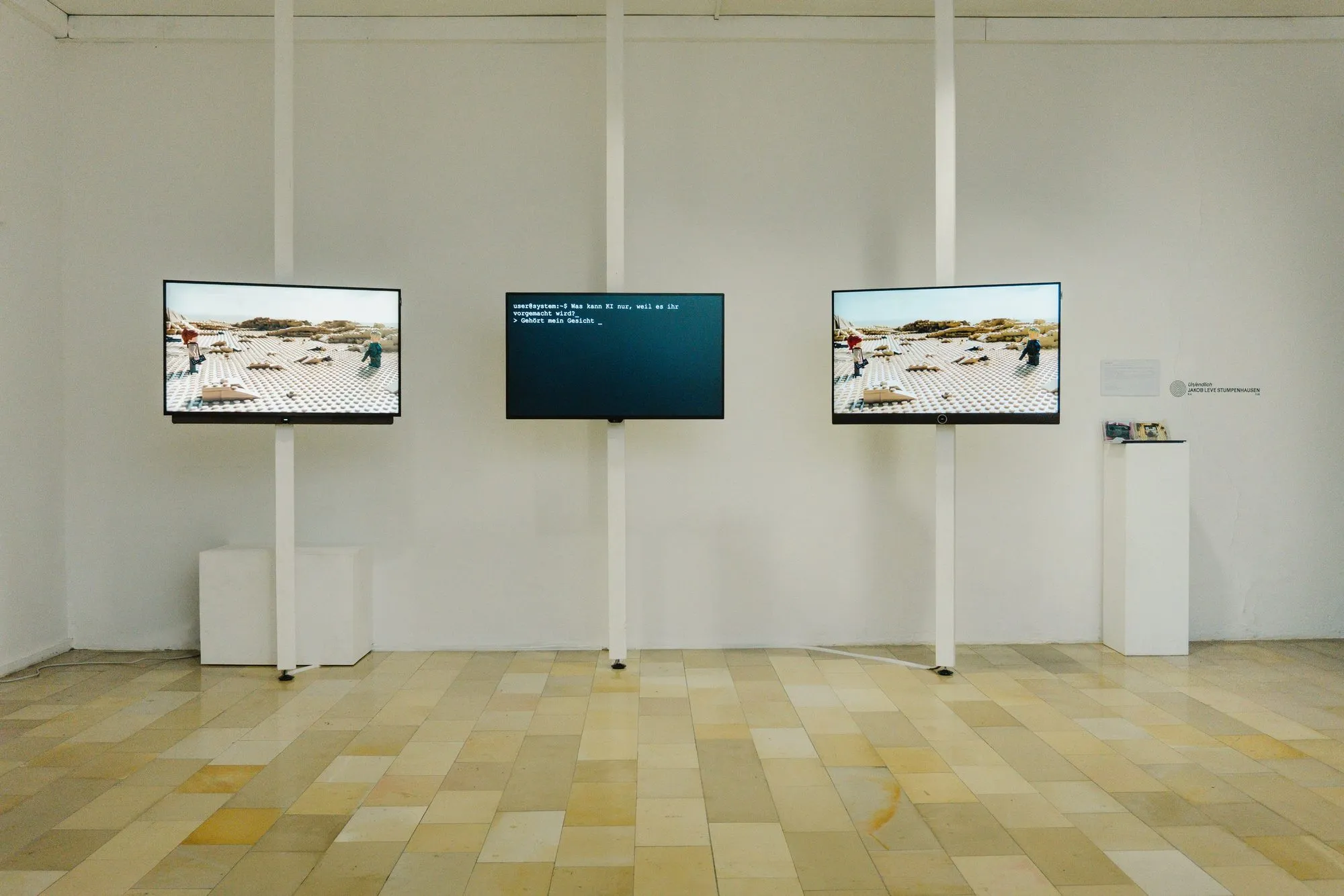Drei Bildschirme an einer Wand in einem Ausstellungsraum.