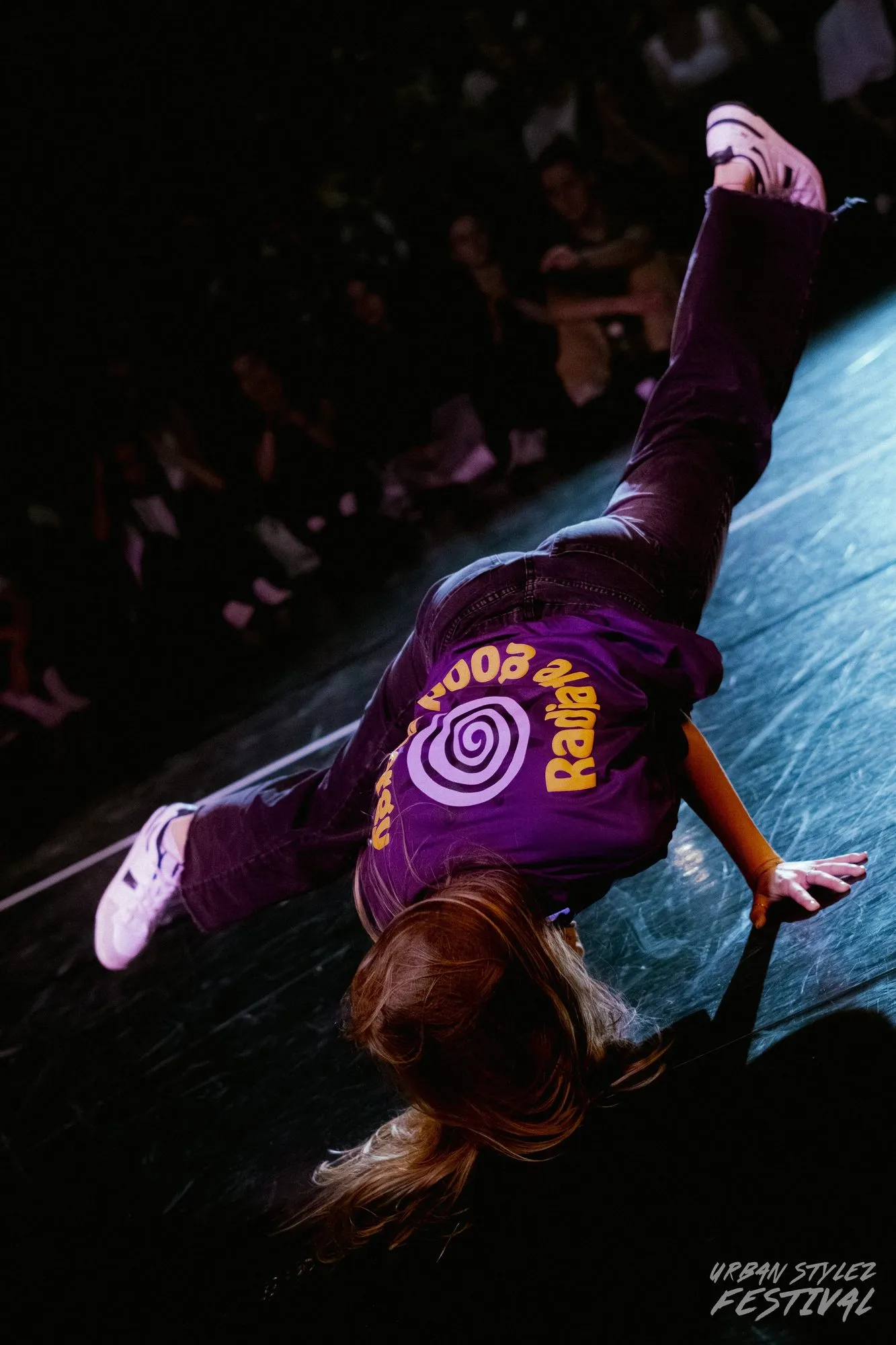 Eine Person in einem Breakdance-Move, kopfüber, vor blauem Bühnenlicht.