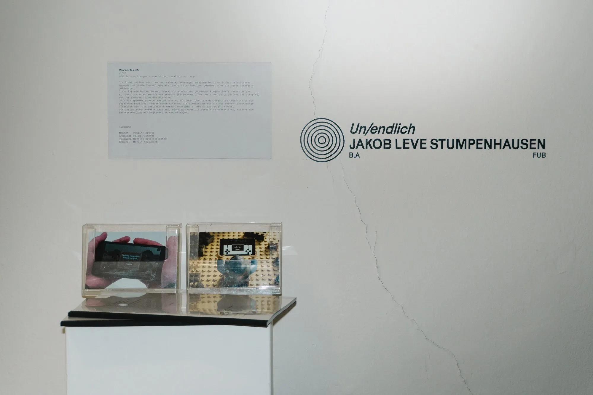 Wandtafel der Ausstellung mit dem Titel Un/endlich, darunter zwei Objekte in Vitrinen.