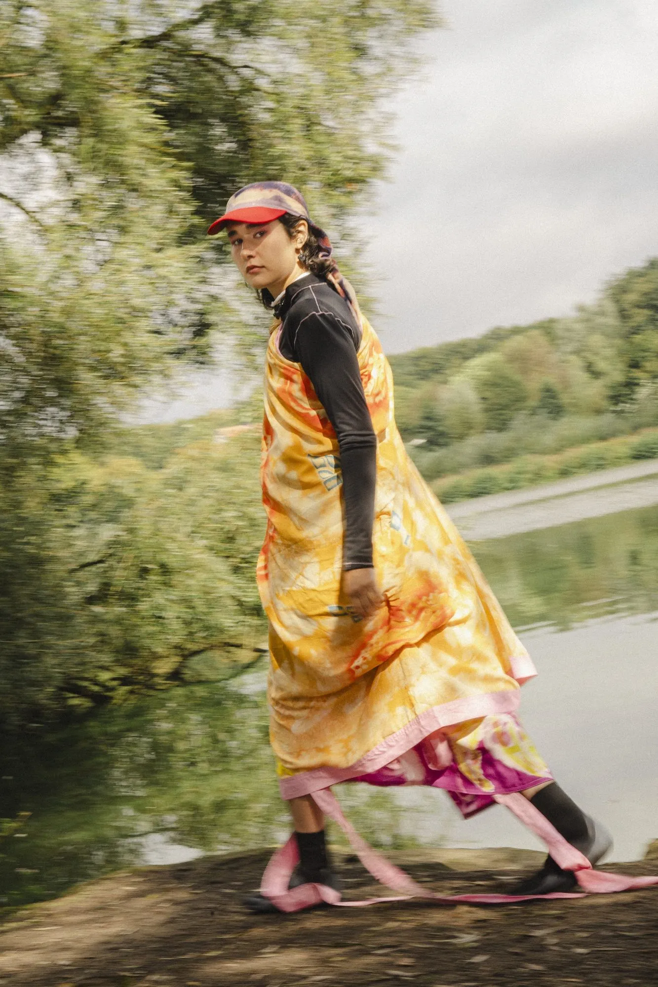 Eine Person in gemustertem Kleid geht einen Weg am Wasser entlang, der Hintergrund ist von der Bewegung unscharf.